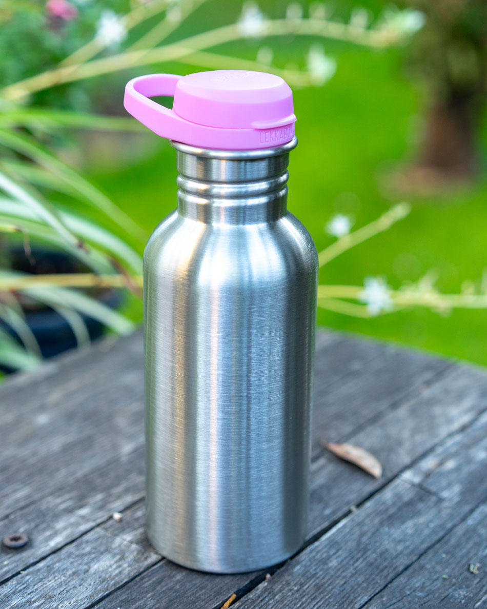 LEKKABOX Go Edelstahl Trinkflasche mit rosa Deckel auf einem Gartentisch